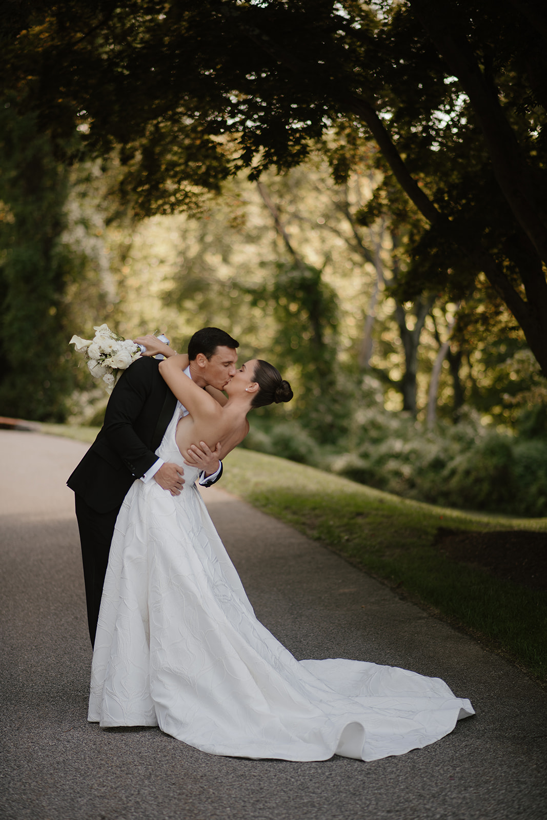 Groom dipping and kissing the bride during a romantic portrait session on a shaded path.